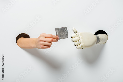 cropped image of woman and robot holding condom through holes on white