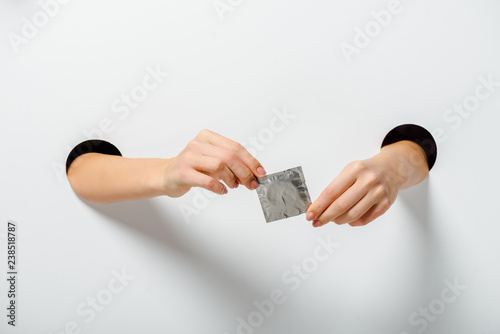 cropped image of woman holding condom through holes on white