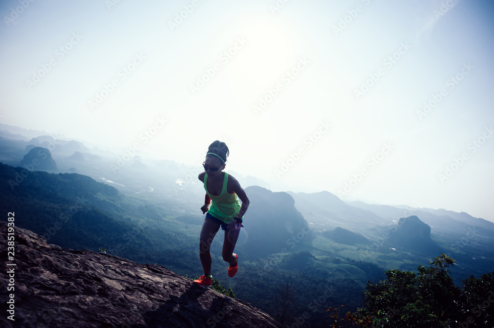 Young fitness woman trail runner running up at mountain top cliff edge
