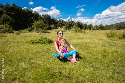 little daughter, four years old girl, resting sitting on her mother legs in a grass meadow of the country in Canencia mountain (Madrid, Spain, Europe)