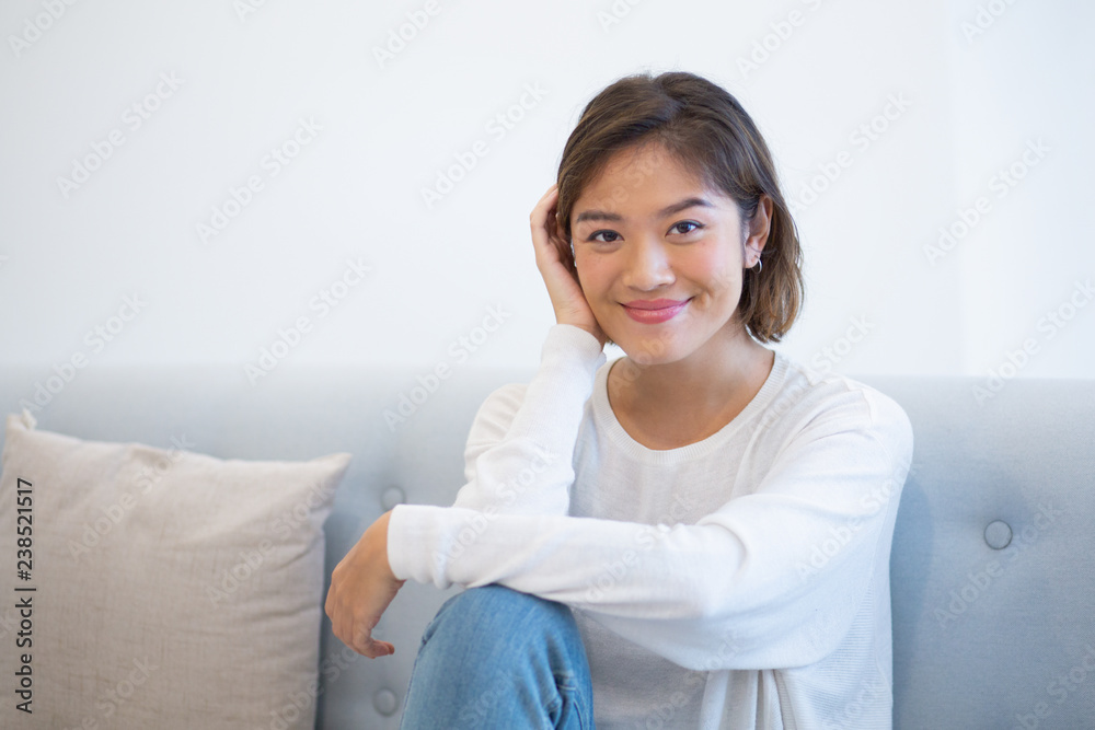 Carefree young woman sitting on coach at home. Portrait of beautiful Asian girl posing indoors. Beauty concept Carefree young woman sitting on coach at home. Portrait of beautiful Asian girl posing indoors. Beauty concept
