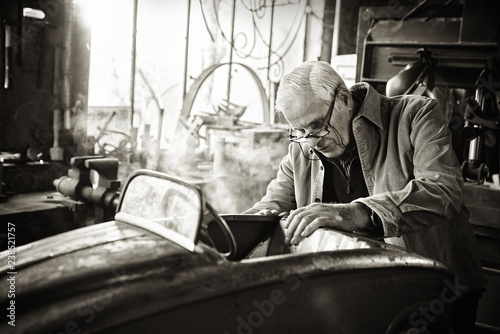 Senior man in his workshop repairing an old fashioned pedal car 