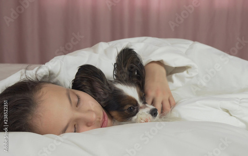 Beautiful teen girl sleeping sweetly in bed with Papillon dog © Julia Mashkova