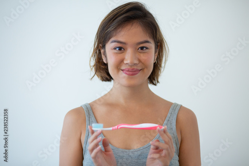 Portrait of smiling young woman holding toothbrush. Asian girl advertising new toothbrush. Dental care concept