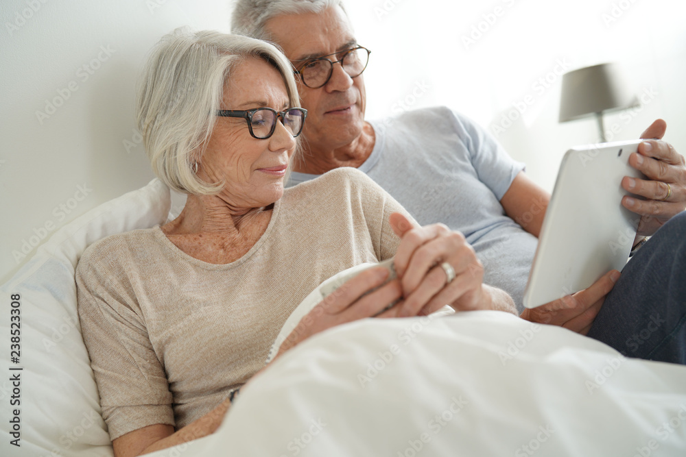Senior married couple relaxing in bed looking at tablet Senior married couple relaxing in bed looking at tablet