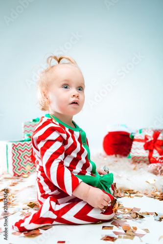 Cute baby girl 1 year old near santa hat posing over Christmas decoratins. Sitting on floor with Christmas ball. Holiday season. photo