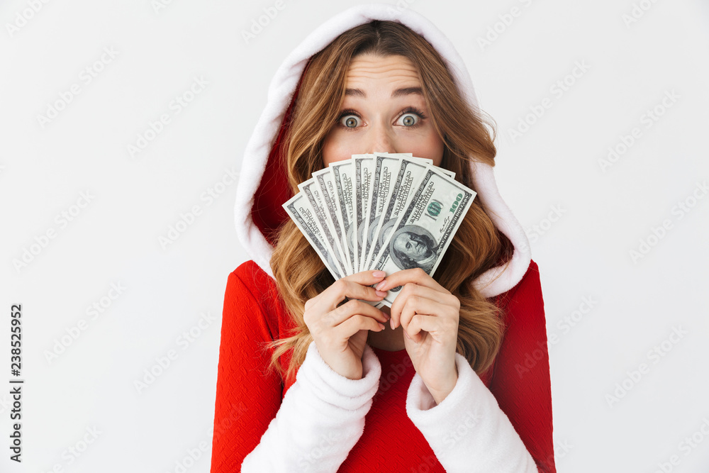 Portrait of caucasian woman 20s wearing Santa Claus red costume smiling and holding fan of money in dollar banknotes, isolated over white background Portrait of caucasian woman 20s wearing Santa Claus red costume smiling and holding fan of money in dollar banknotes, isolated over white background