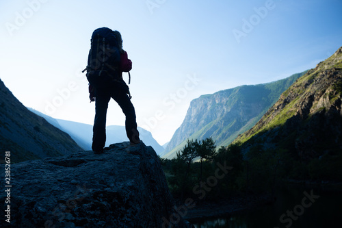 Woman hiker stands with backpack on the rock and enjoys the mountains view. Altai, Russia