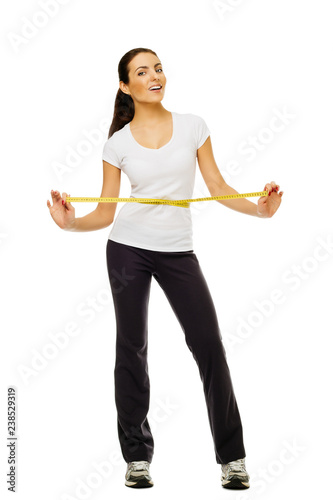 Young woman measuring her waistline with a measuring tape over white background.