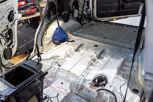Disassembled car body, inside a white SUV, with parts and interior elements removed, prepared for the restoration and replacement of sound insulation and interior trim.