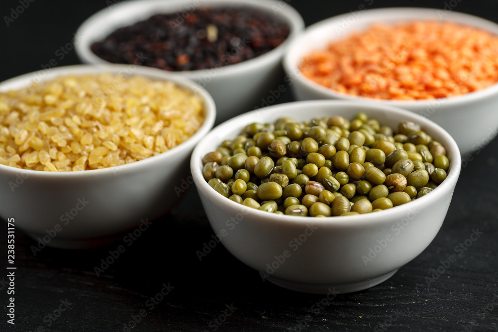 Set of different cereals and legumes in a white bowls on a black table Set of different cereals and legumes in a white bowls on a black table