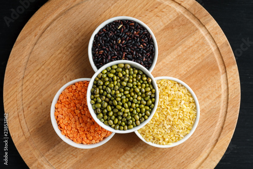 Set of different cereals and legumes in a white bowls on a black table, top view