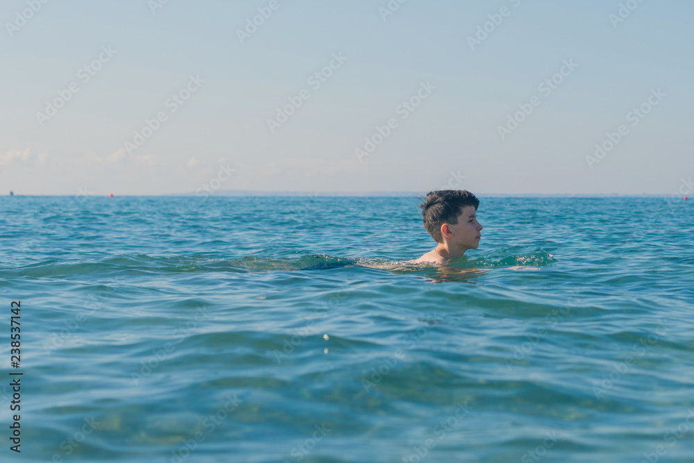 Happy and smiling teen boy swimming in the sea. Travel and summer concept