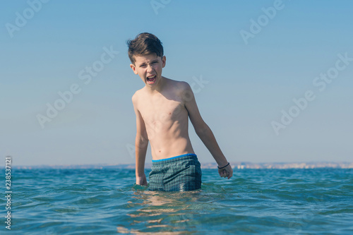 13 years old boy throws up his hands and screaming in the sea waves. Concept of family summer vacation