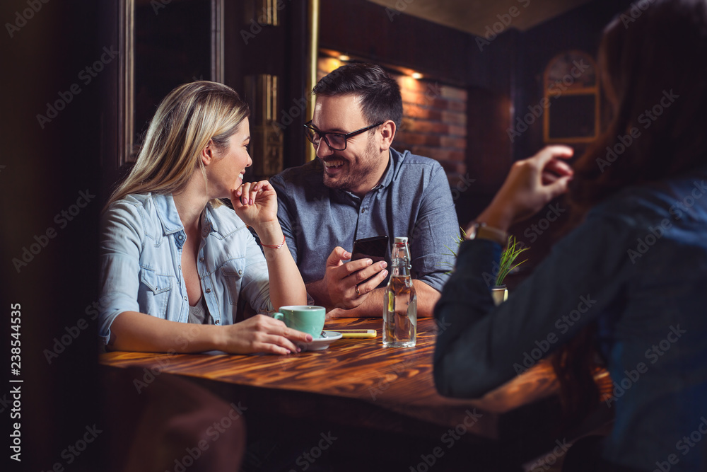 Fototapeta premium Handsome male holding a phone and looking at his girlfriend. Enjoying time in pub.