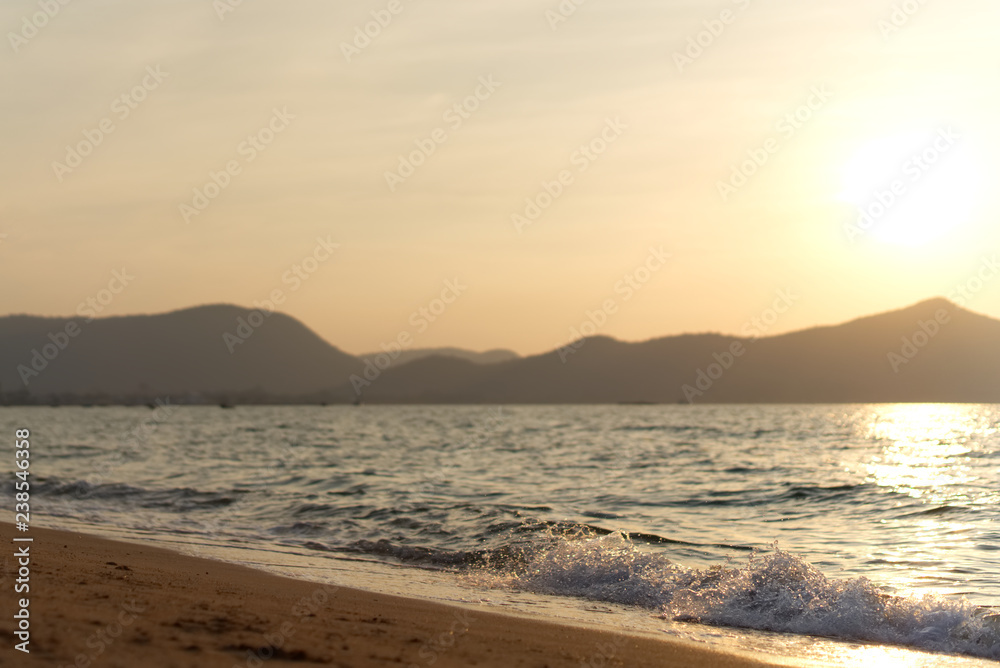 Wave is coming to the beach. Seen in beautiful sunset on the beach in the evening. Background is sun falling down behind the mountain. Happy holiday and vacation concept.