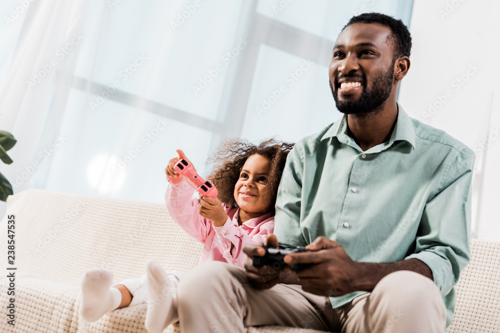 african american dad and daughter playing video games in living room african american dad and daughter playing video games in living room