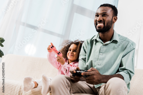 african american dad and daughter playing video games in living room