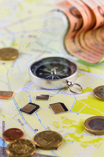 Close-up gsm cards of different sizes lie on the city map surrounded by coins, Euro banknotes and compass