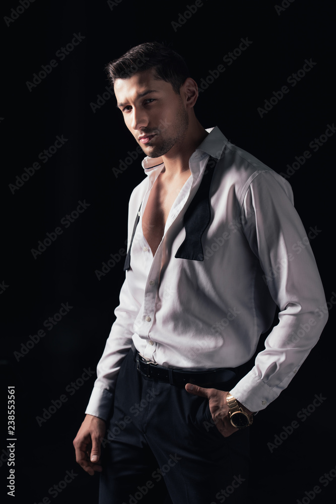 Fototapeta premium handsome man in white shirt and hand in pocket looking at camera while posing isolated on black
