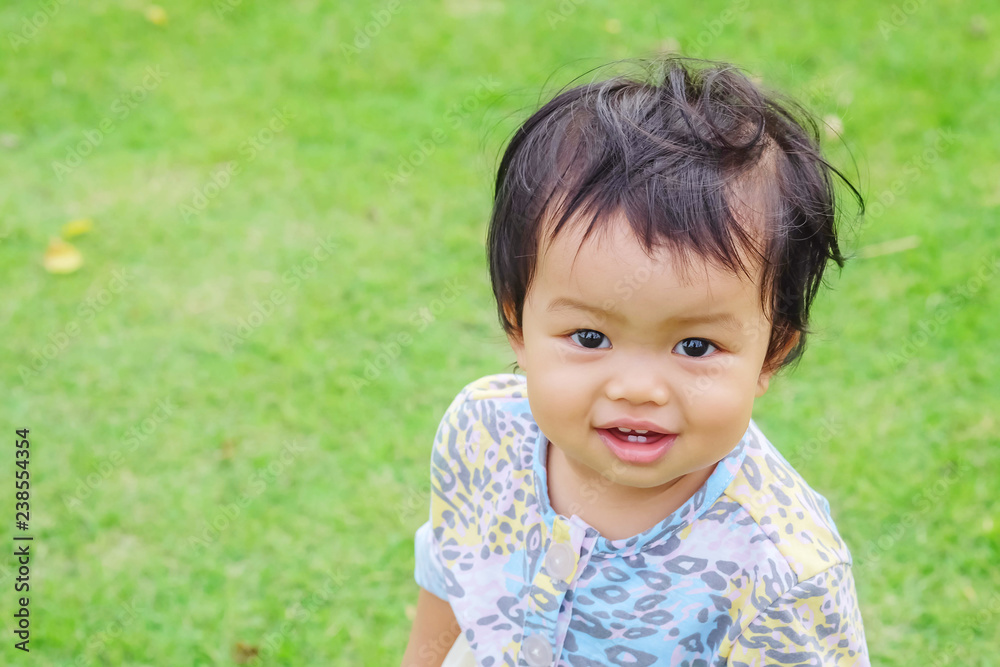 Closeup little girl with smile face stand on grass floor in the park background with copy space Closeup little girl with smile face stand on grass floor in the park background with copy space