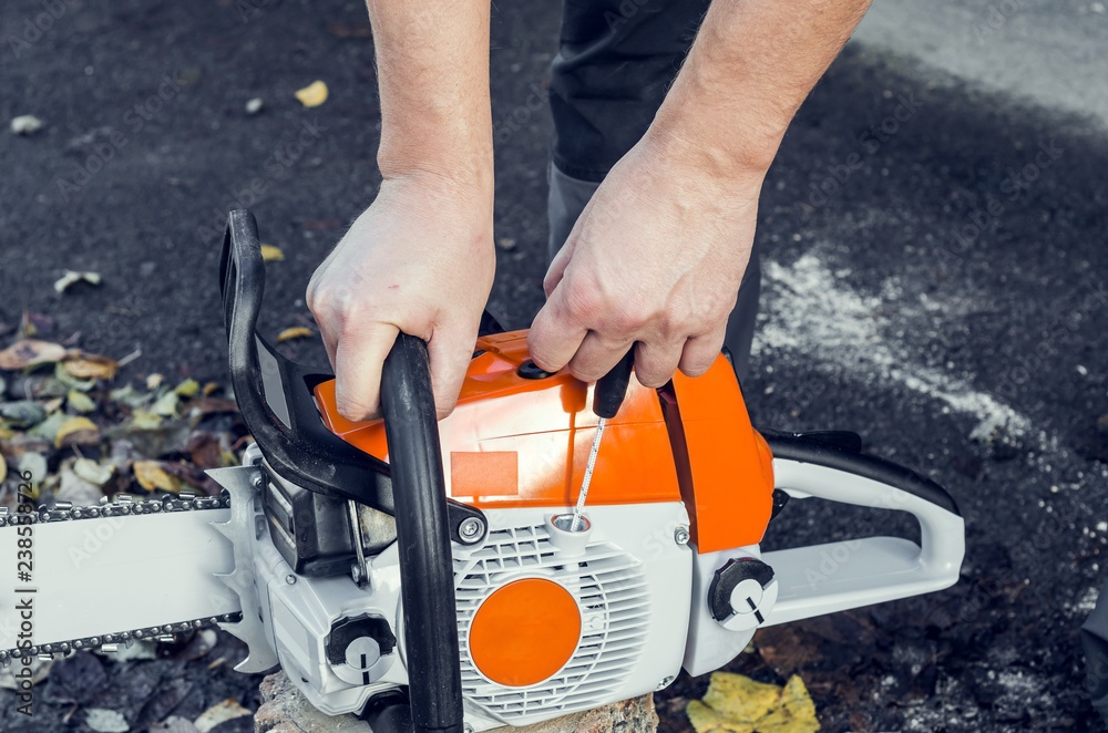 Man's hand starts a chainsaw starter to the back yard