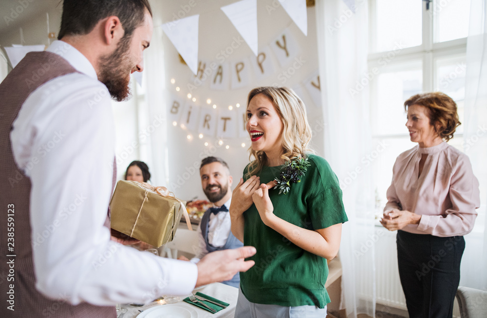 Obraz premium A man giving gift to a young surprised woman on a family birthday party.