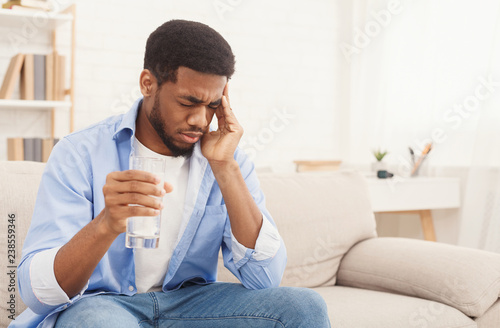 African-american man with headache taking pill at home