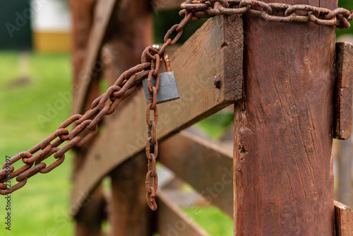 Padlock with a chain rusted on a wooden fence with grass background with selective focus on the padlock