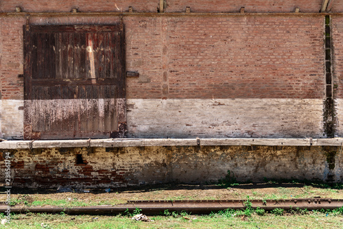 Sliding wooden door of a barn or deposit with a brick wall to write something and old railways down with green grass