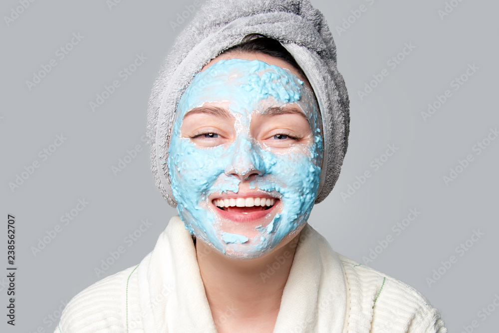 Fototapeta premium Woman applying facial clay mask at spa salon or at home, skincare theme. Face mask, spa beauty treatment with copy space on gray background.