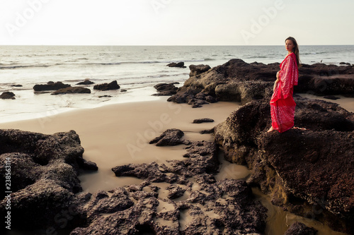 indian female model in vacation on paradise tropical beach by ocean sea. hindu woman with kundan jewelry traditional India costume red wedding sari.asian girl near the rocks shores of Indian Ocean bay photo