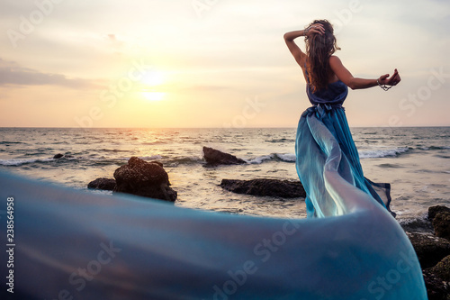 Foto gorgeous style brunette young woman in blue chameleon dress long train standing on a rock near the sea, sand tropical on a rock