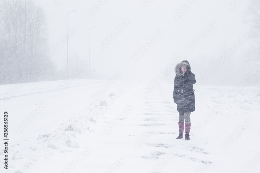 Winter is coming by snow. Poor visibility in heavy snow storm on path. Woman slowly and hard walking in dangerous weather day. Cataclysm of nature. City people life in blizzard concept.