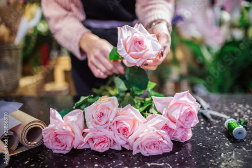 Close of beautfiul light pink roses lying on table. Florist hold one flower in hand. Paper rolld and coil with green thread are on table. photo