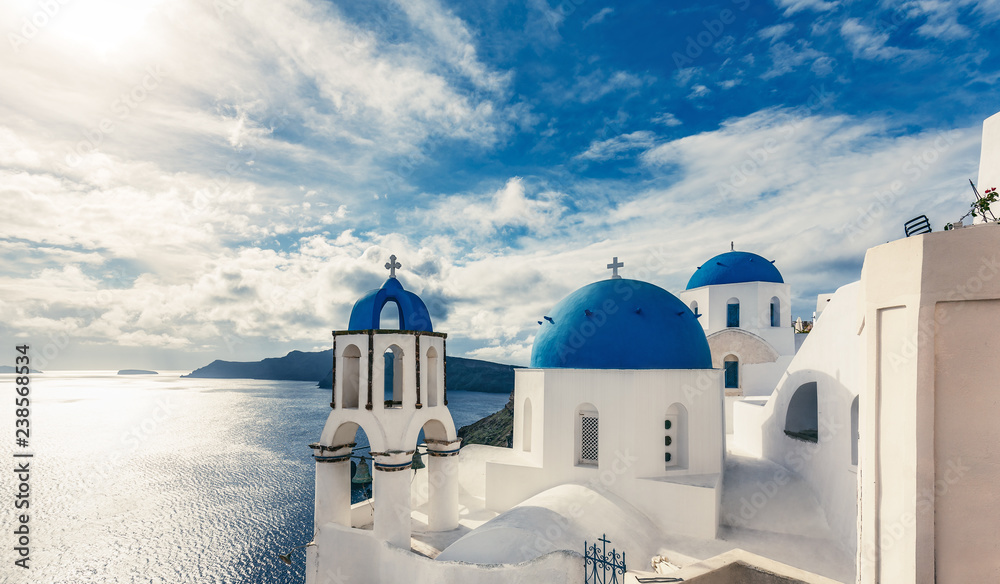 Churches in Oia, Santorini island in Greece, on a sunny day with dramatic sky. Scenic travel background.