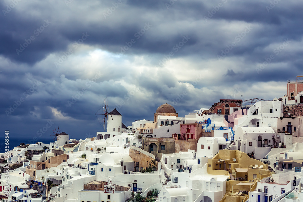View over Oia village, Santorini island in Greece, on a sunny day with dramatic sky. Scenic travel background.