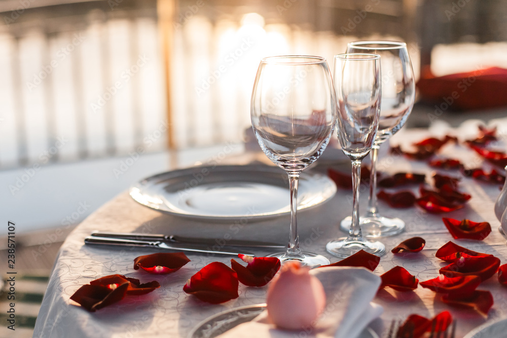 Romantic Valentine day dinner setting  with rose petals and empty wineglasses on sunset
