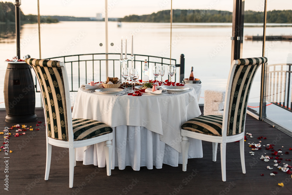 Obraz premium Romantic Valentine day dinner setting with rose petals and empty wineglasses on sunset