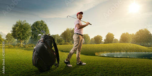 Male golf player on professional golf course. Smiling golfer walking on fairway with golf bag and club photo