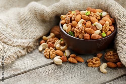 Wooden bowl with nuts on a wooden background, near a bag from burlap.