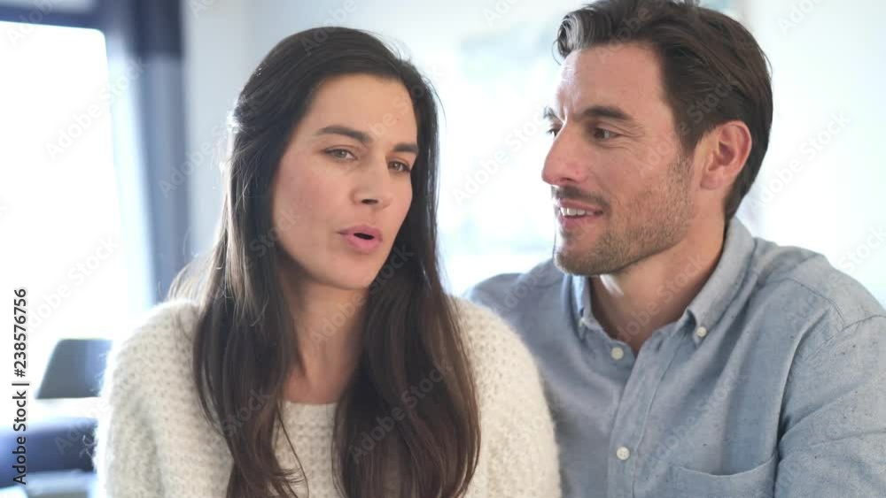 Attractive couple facing and talking to camera in modern home Attractive couple facing and talking to camera in modern home