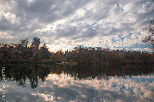 Panoramic view of the Ticino river with clouds and trees that are reflected in its clear water, on a winter day at sunset. © serghi8