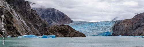 Gorgeous panoramic view of Sawyer Glacier with a boat sailing it and icebergs floating next to it in Alaska's Tracy Arm Fjords Terror Wilderness