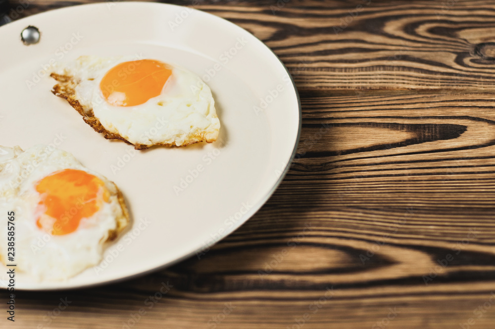 Two fried eggs in metal beige pan on old wooden brown table. Copy space Two fried eggs in metal beige pan on old wooden brown table. Copy space