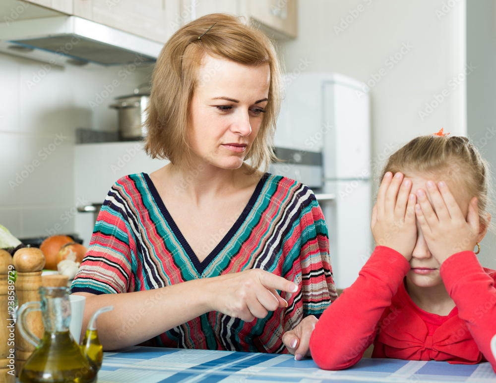 Fototapeta premium woman lecturing small female child in the kitchen
