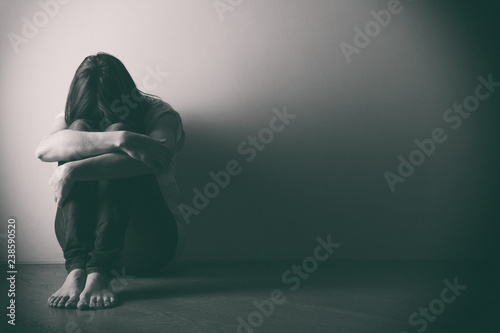 Teenager girl with depression sitting alone on the floor in the dark room. . Black and white photo