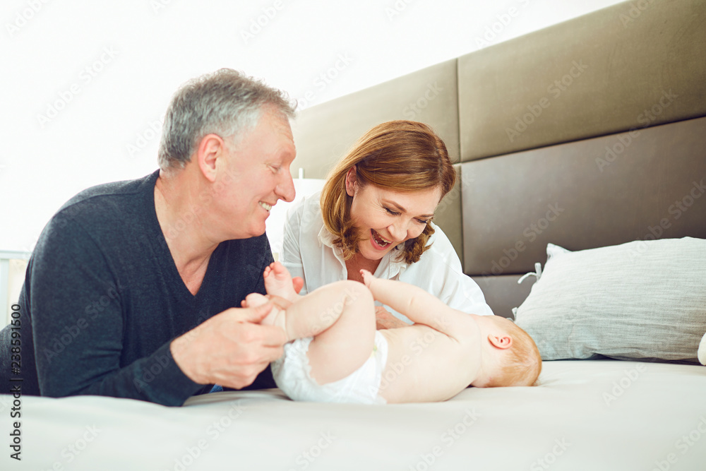 Grandparents and the baby are playing on the bed . Grandparents and the baby are playing on the bed .