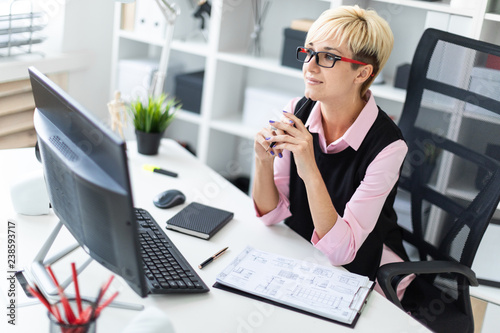 A young girl is sitting at a Desk in the office and leaned a pencil to her chin.