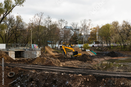 Big excavator during earthmoving works outdoors at construction site. Yellow excavator clears the river bed for the device pond. All-Russian exhibition center, Moscow. Russian Federation.